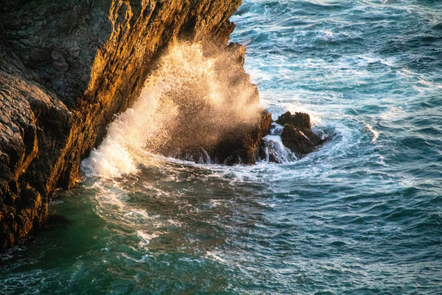 Ocean waves crashing on rock cliff-face in sunshine