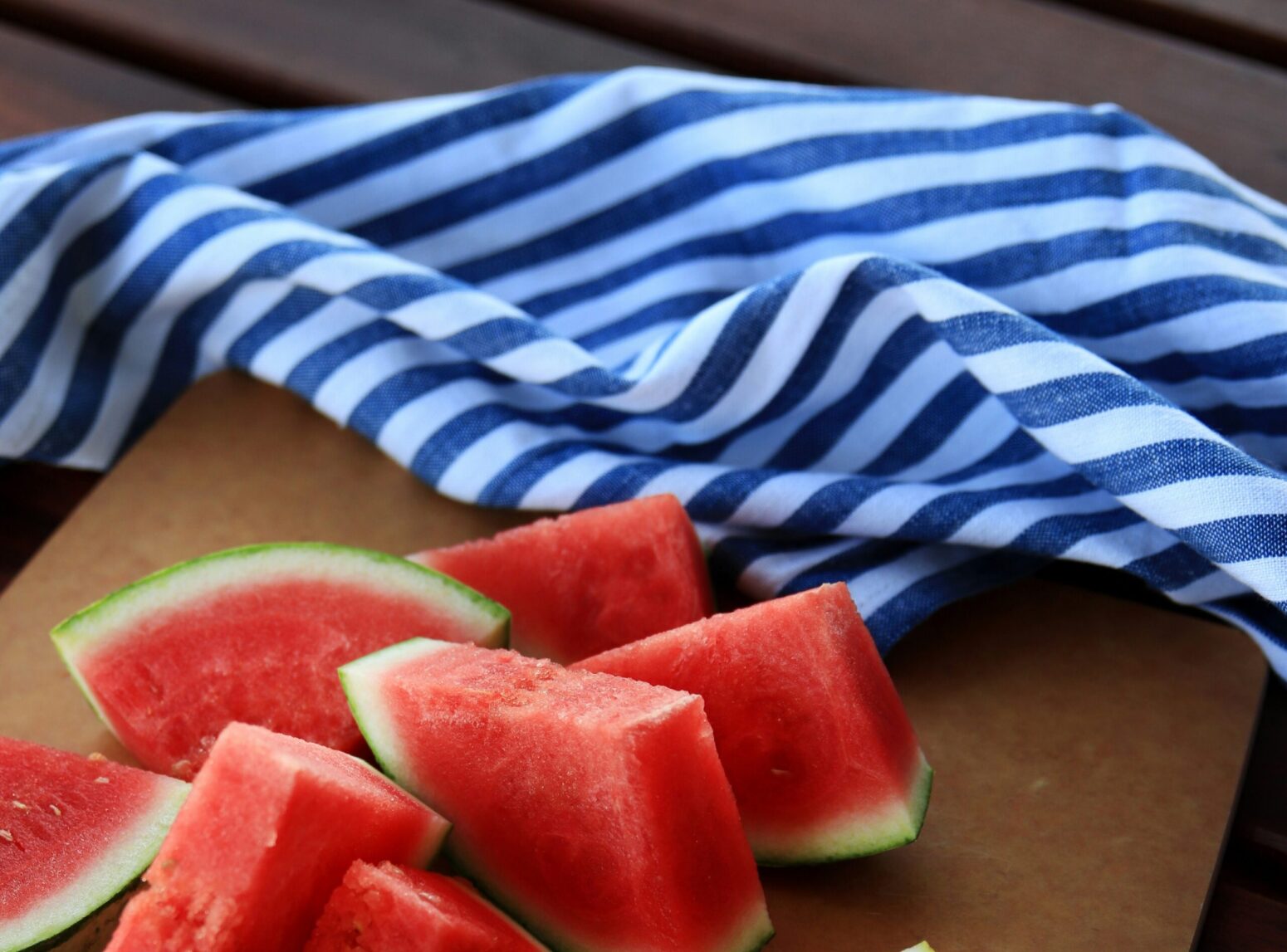 Sliced watermelon sitting on a piece of cardboard next to a blue-and-white-striped blanket