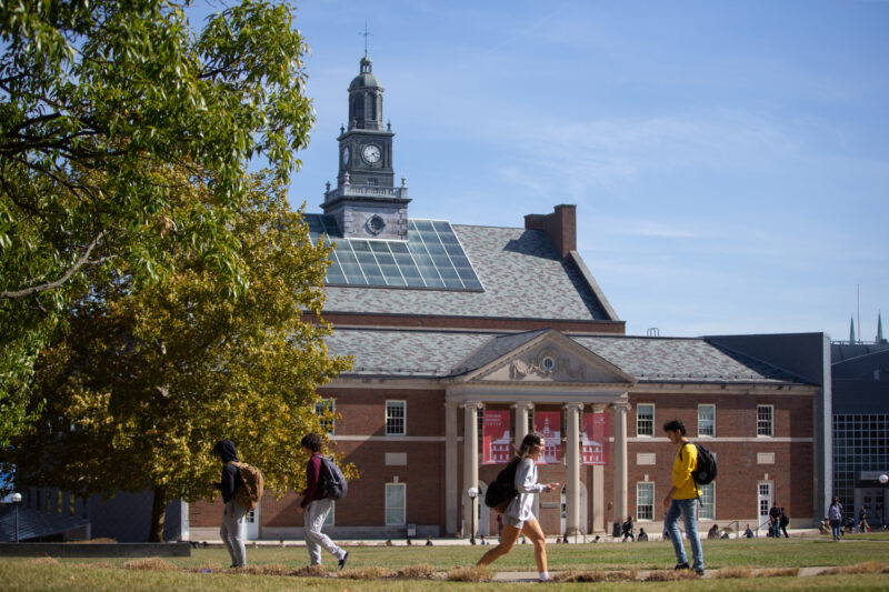 Students walk on a green lawn in front of the student union building on the UC campus.