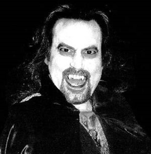 A black-and-white photo of Count Cool Rider, with long hair and a goatee as well as ghoulisth makeup on and fake vampire teeth