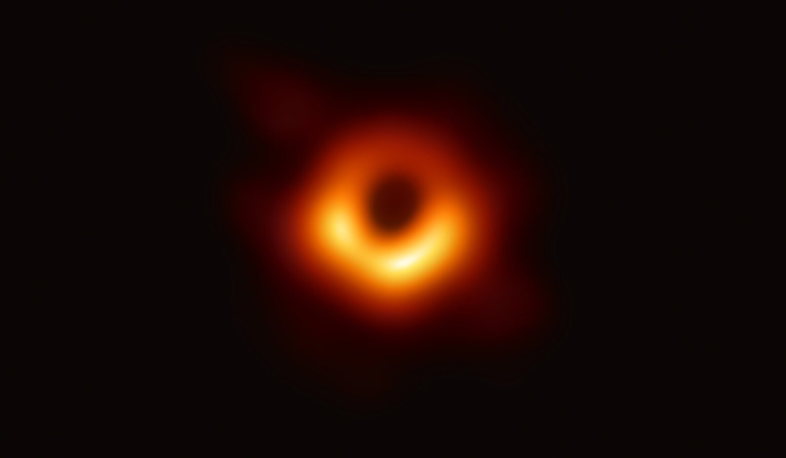 NASA's first image of a black hole. What looks like an orange eye with a black iris at its center sits alone on a black plane.