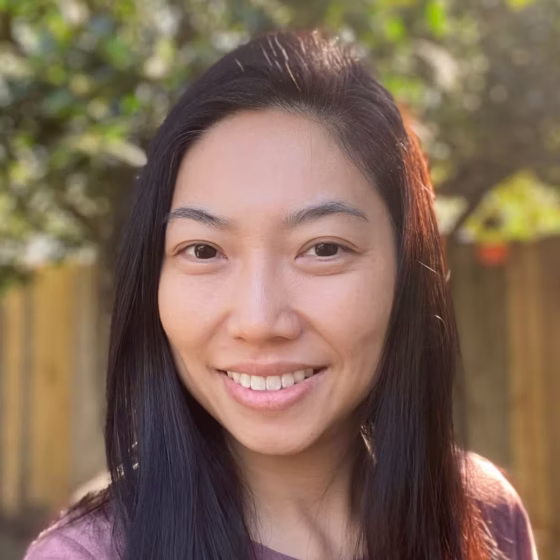 M. Cynthia Cheung, an Asian-American woman with long hair, smiles in a backyard-type setting.