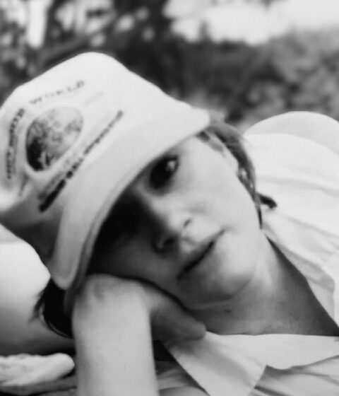Gabrielle Frahm-Claffey, a white woman, wears a baseball cap and rests her head on one hand in a park-like setting. The photo is black-and-white.
