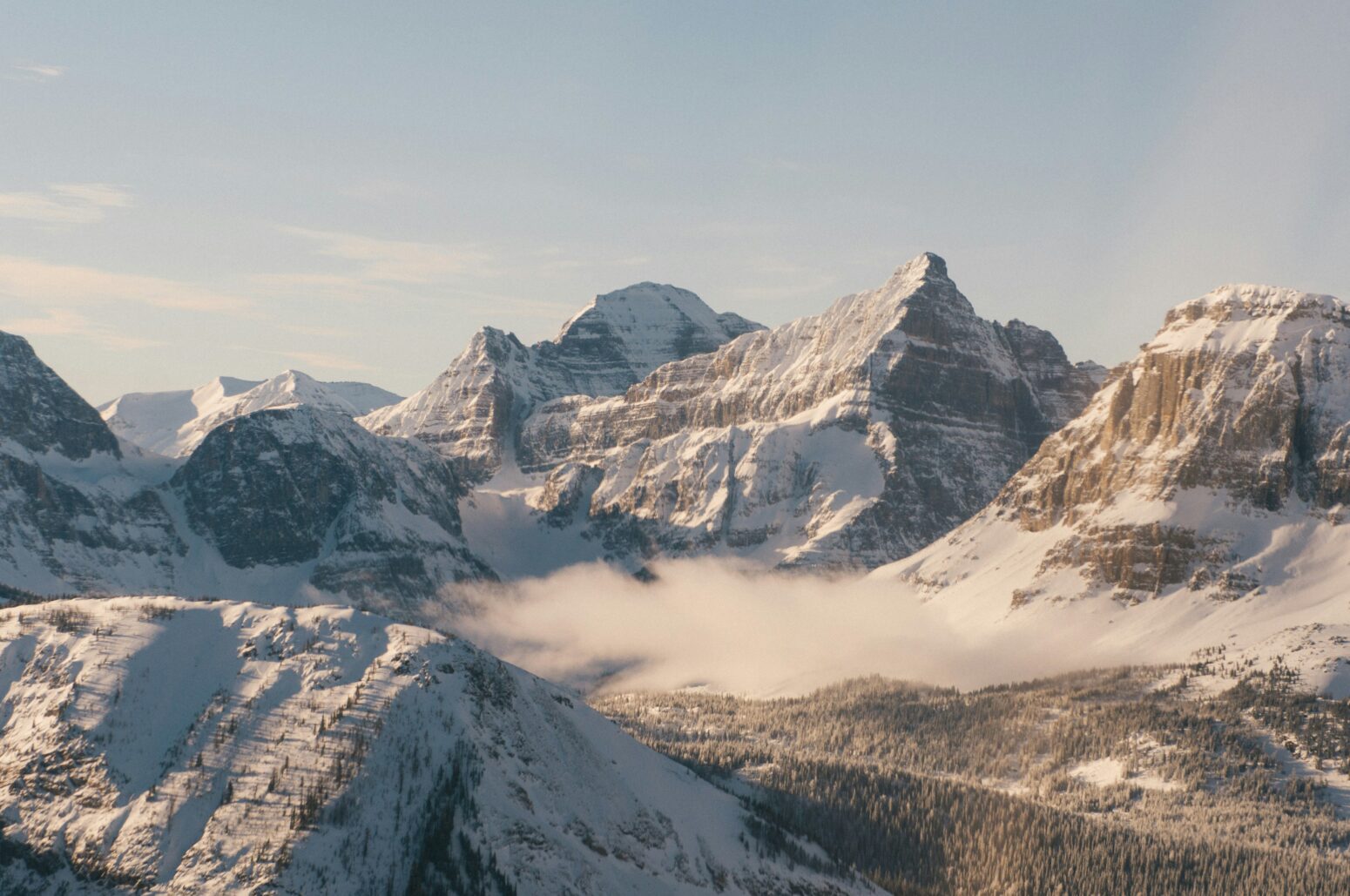 View of the Rockies capped with a dusting of snow and a low-hanging cloud between peaks. The sky above the mountains is grayish.