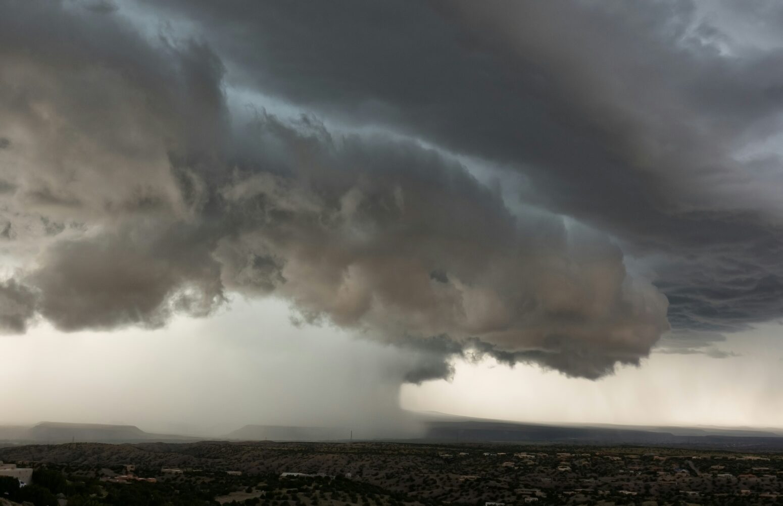 A monsoon-level shower falls from a fluffy cloud into a valley full of trees.