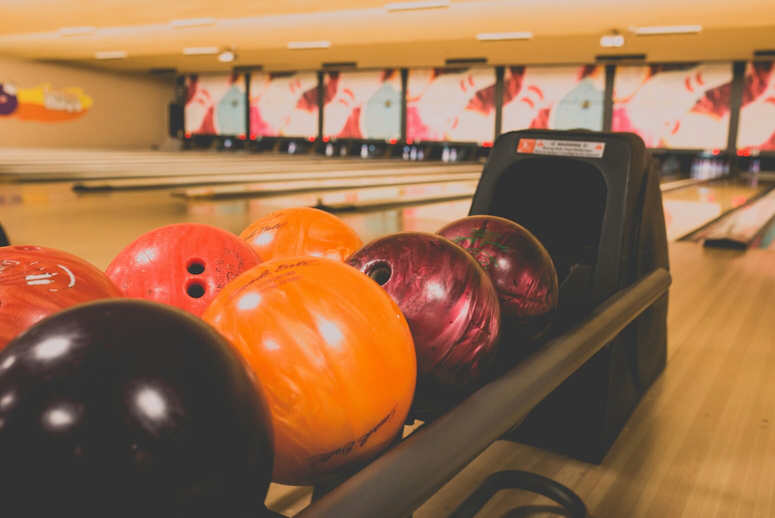 Brightly colored bowling balls are lined up in a bowling alley.