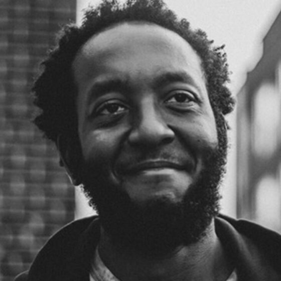 Raphael "Ralph" Jenkins, a Black man with a beard, smiles peacefully at a point above the camera. The photo is black-and-white.