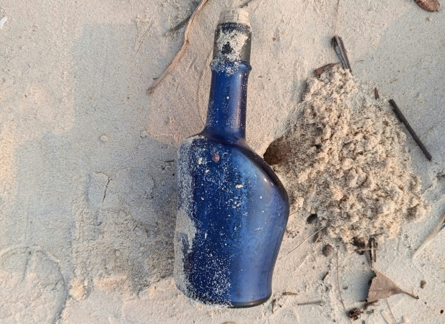 A blue, corked bottle sits on a bed of sand.