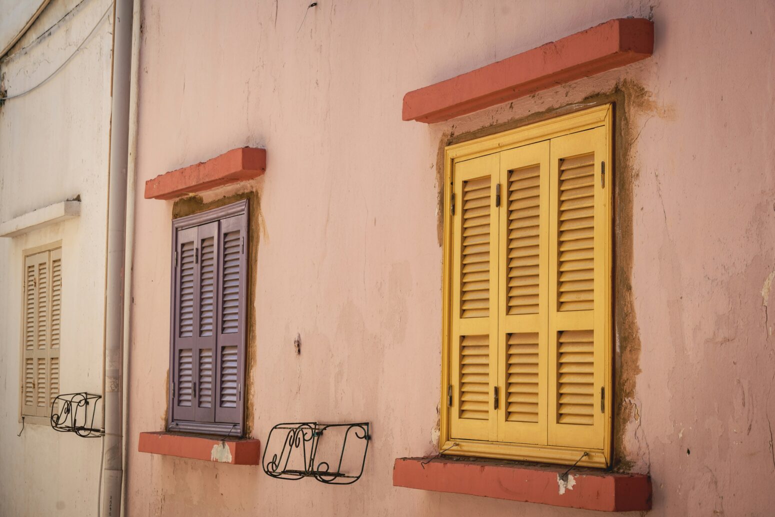 Colorful shutters on the windows of a tan-colored building in Tyre, Lebanon. The shutters are butter yellow and French blue, with terra cotta frames.
