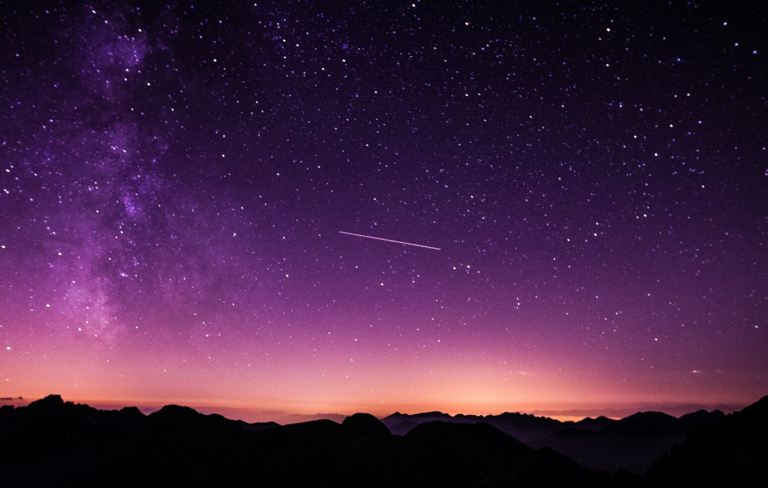 A comet streaks through a pink and purple sky above a treeline.