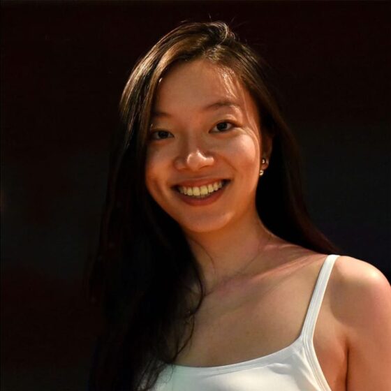 Stella Wong, an Asian woman with long hair hung over one shoulder, wears a tank top and smiles down at us. She stands against a black background.