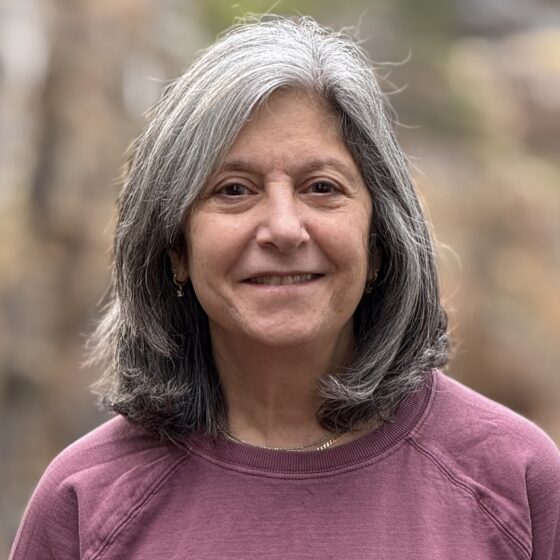 Georgi Bargamian smiles while wearing a dusk-rose colored sweater in front of a naturalistic setting.