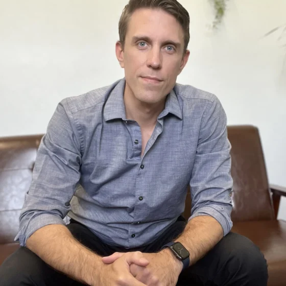 Seth Peterson, a clean-shaven white man with brown hair, sits forward in a leather chair. He wears a chambray button-down and black pants.
