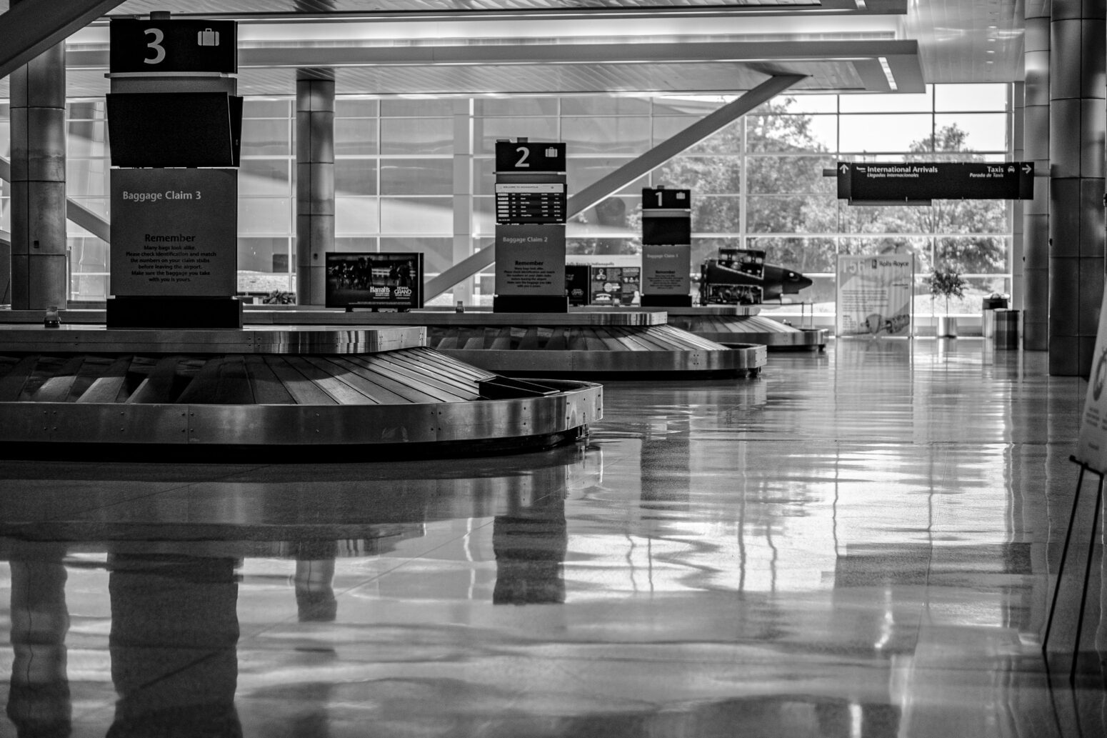 Black and white photo of an empty baggage claim area in an airport, with multiple baggage carousels empty of suitcases.