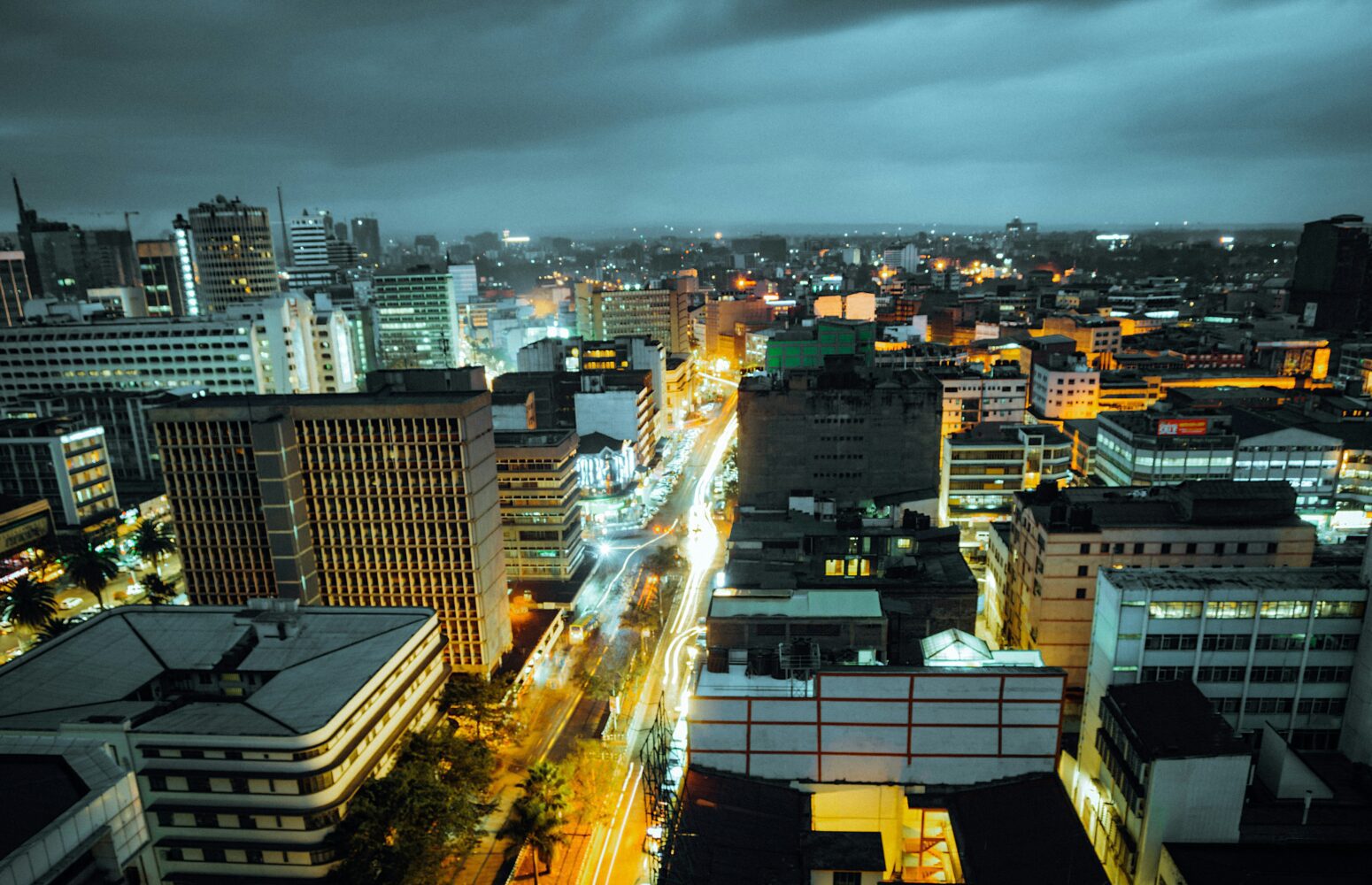 Nairobi cityscape by night: long exposure. Lights glow in buildings below a low, cloudy sky.