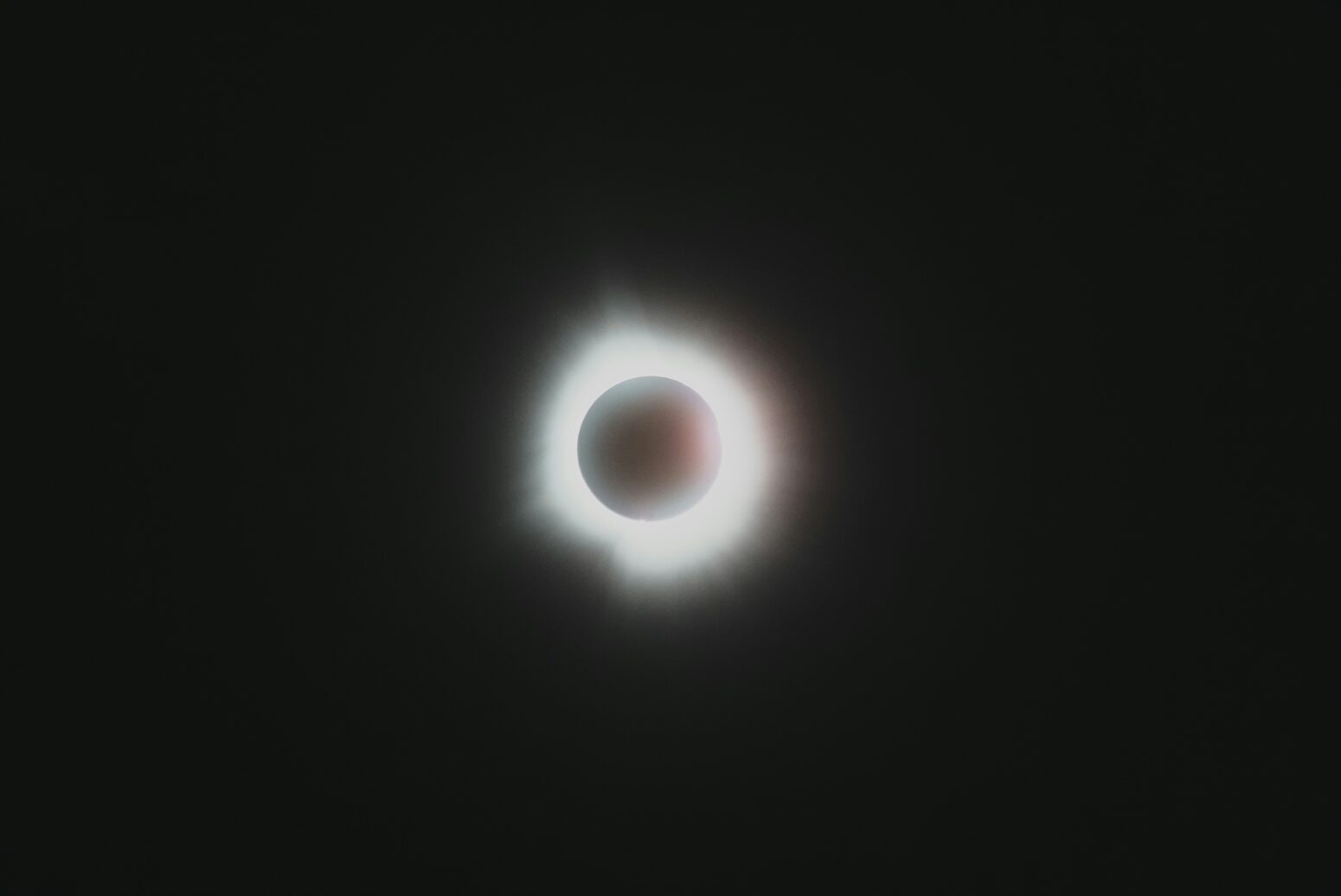 A solar eclipse in a dark sky: black background, with a black circle surrounded by a corona of light in the middle