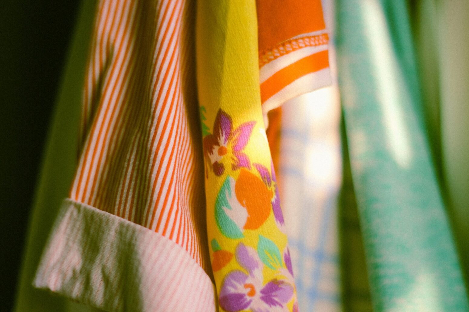 Bright clothes in shades of orange, yellow, and green hang in a closet.