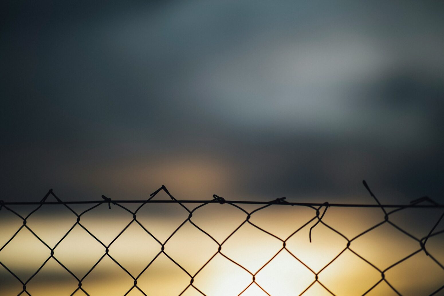 Silhouette of a chain-link fence against a blurred background.