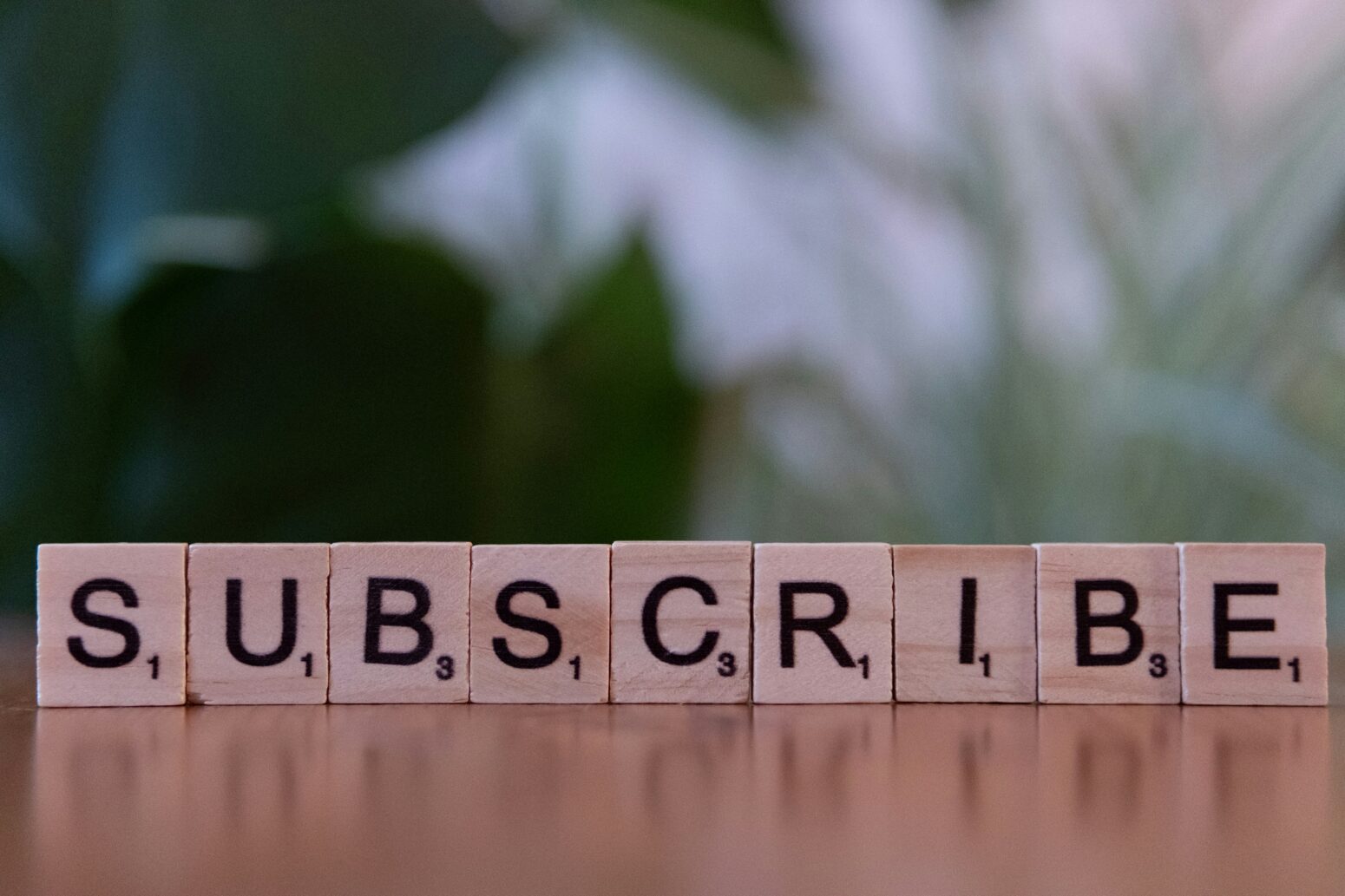 A series of Scrabble tiles lined up on a tabletop to read "Subscribe."