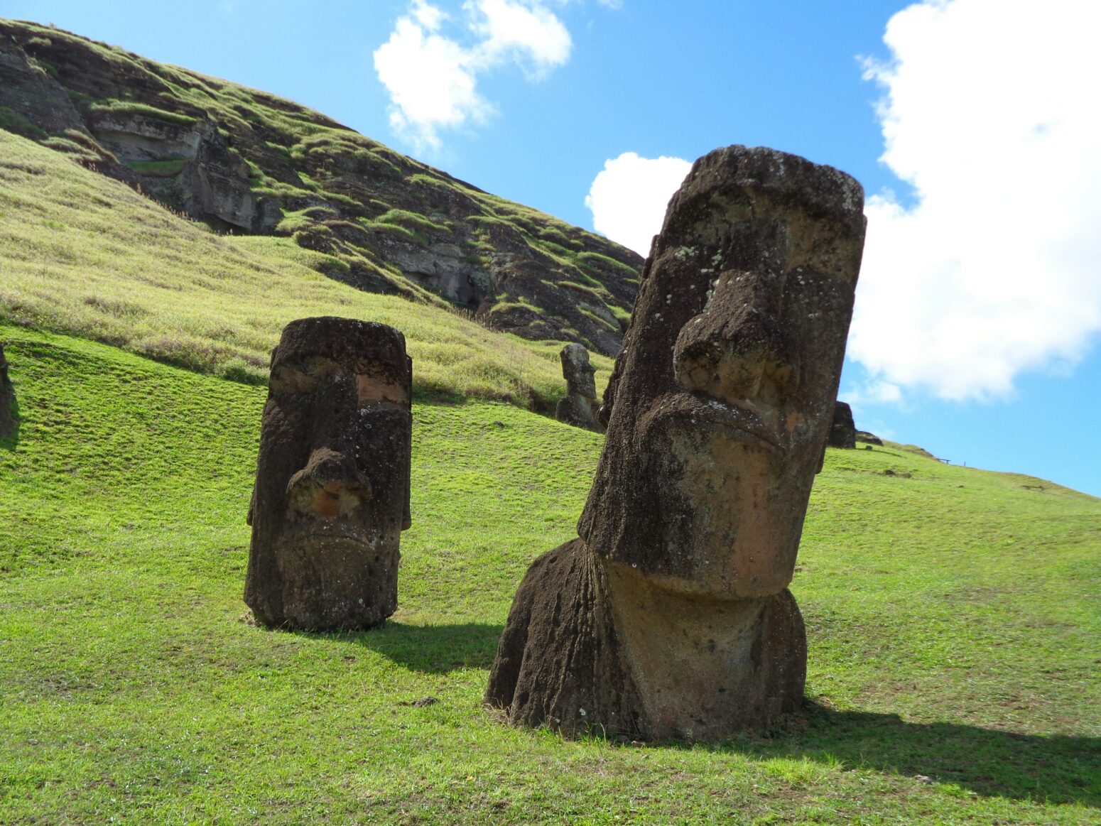Two Easter Island Moai sunk into a green hill: one neck-deep, one shoulder-deep.