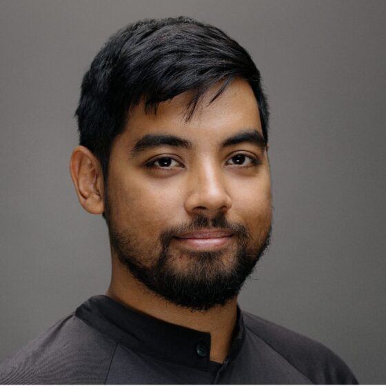 A Southwest Asian man with short hair and a beard, wearing a dark shirt