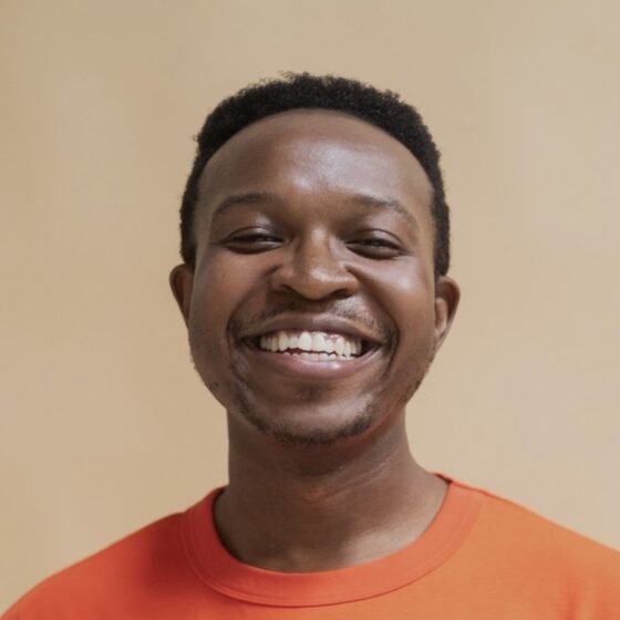 A Black man in an orange shirt, smiling widely