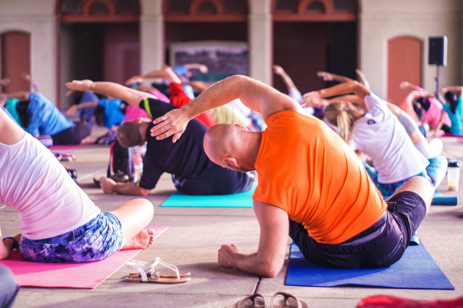 A colorful photo of a full room of people doing yoga, sitting down on mats and leaning over to one side with the other arm up.