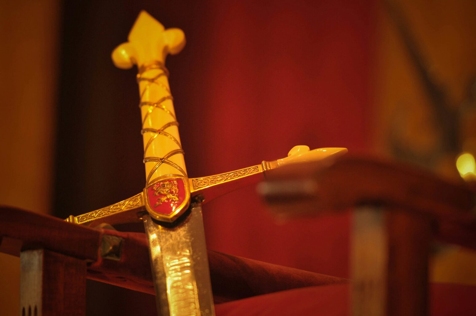 A golden-colored cross-hilted sword with a red crest. It's leaning against something and the background is red