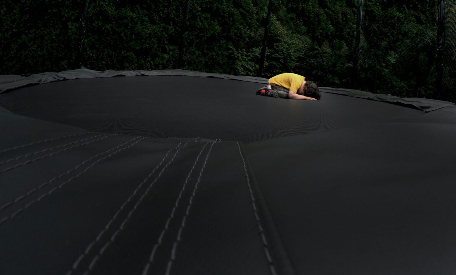 large black trampoline surface with a child in yellow crouched down on it face first