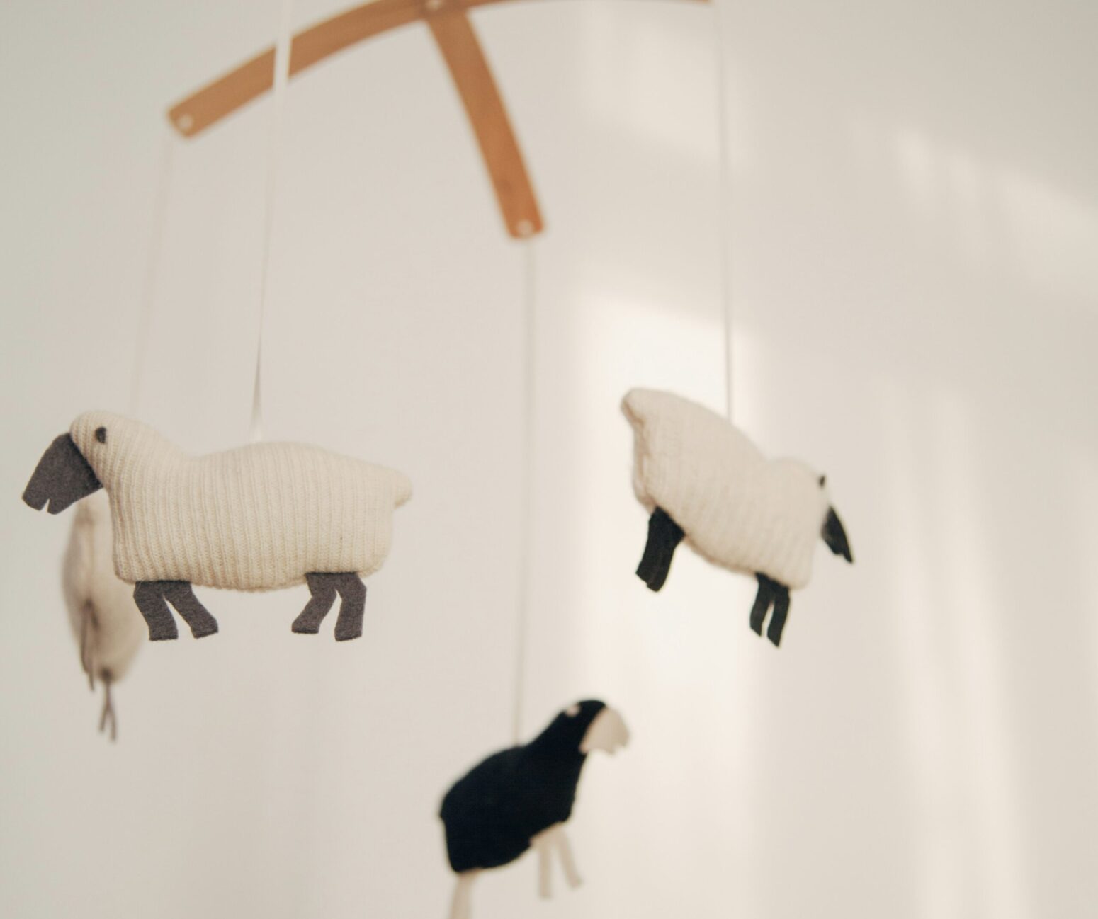 A baby's mobile features four plush corduroy sheep. One is black and the other three are white.