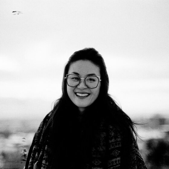 Stephanie Choi stands smiling in an outdoor, naturalistic setting. Choi is wearing eyeglasses and has long, dark hair.