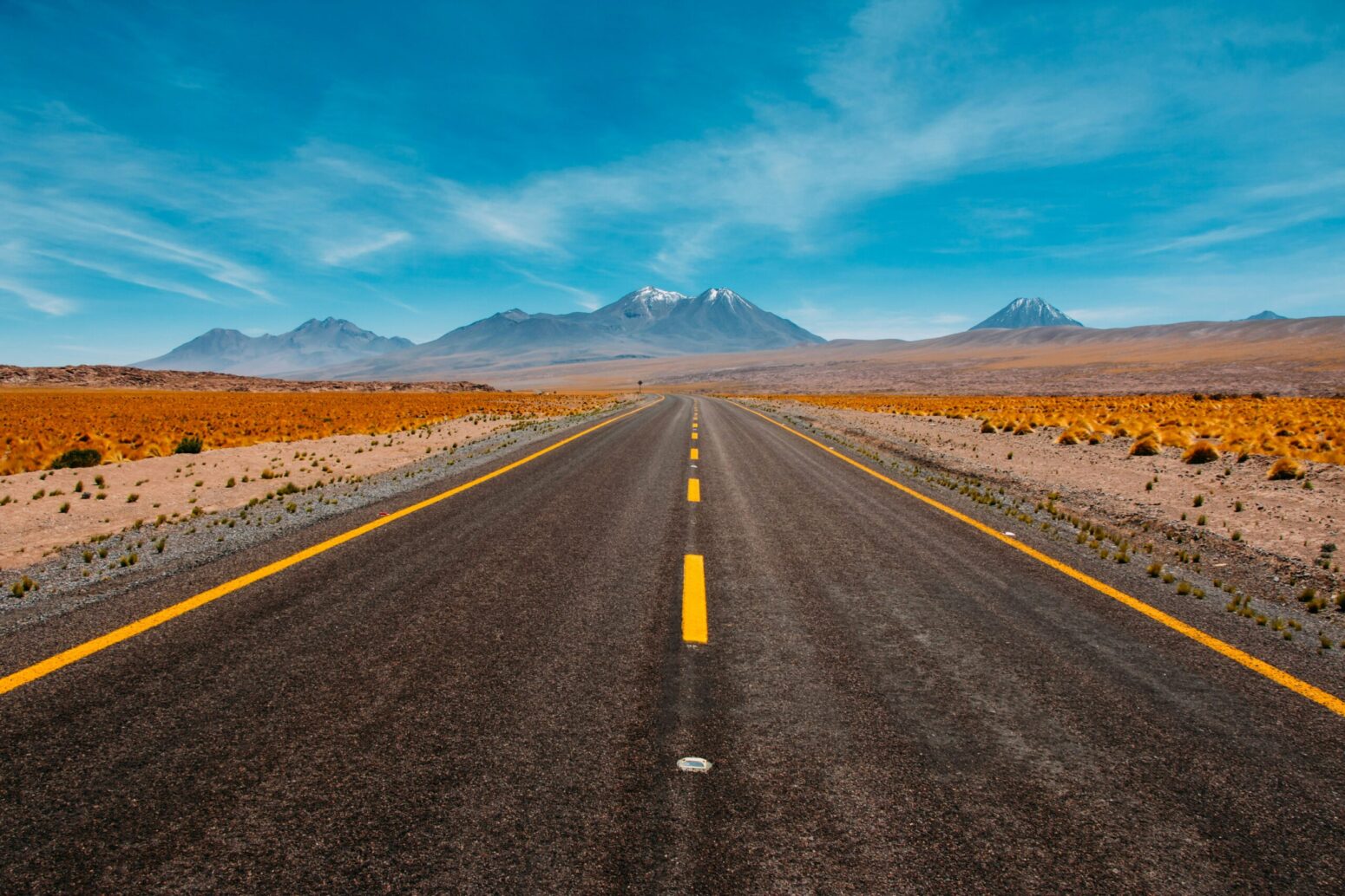 A two-lane road's yellow lines headed toward a mountain range in the distance