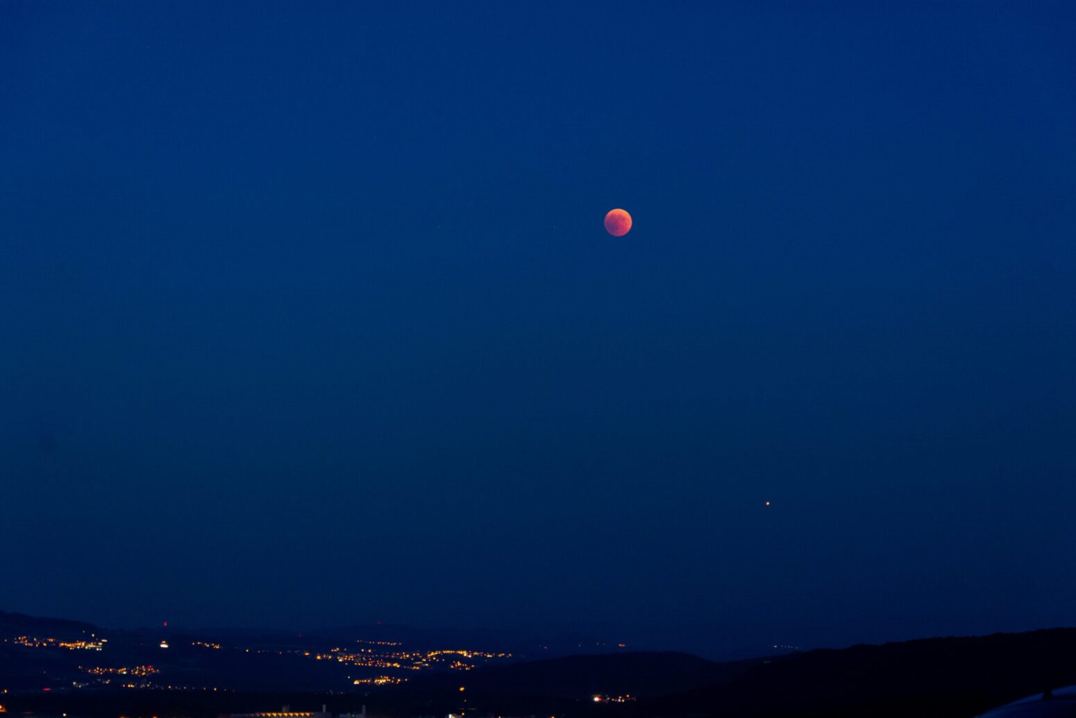 The night sky with some small dots of light to one side. There's a red-colored moon in the top right.