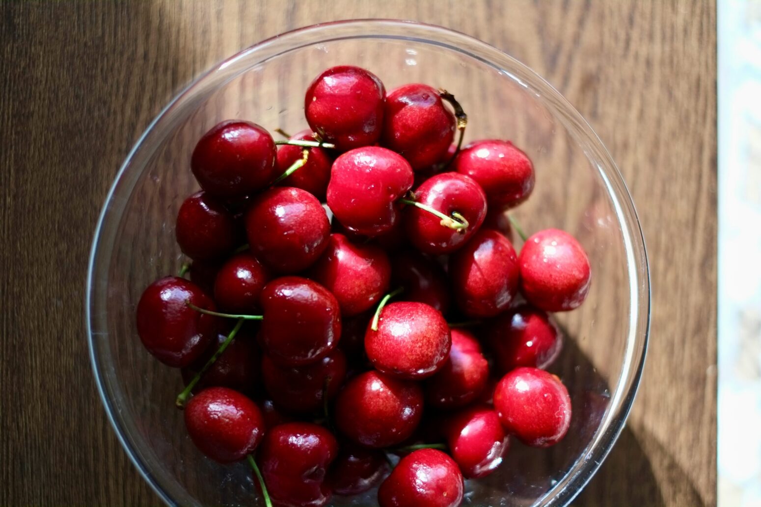 closeup on cherries in a glass bowl on a brown table, partially in sunlight
