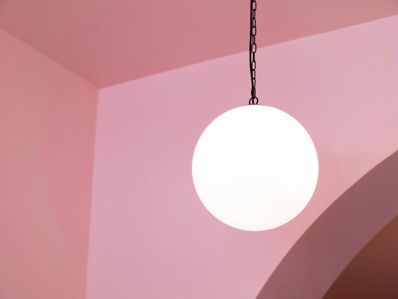 A single round light hanging from the ceiling of a pink painted room