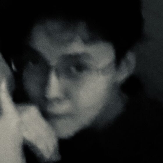An intentionally blurry photo of a Burmese poet with glasses on, in darkness
