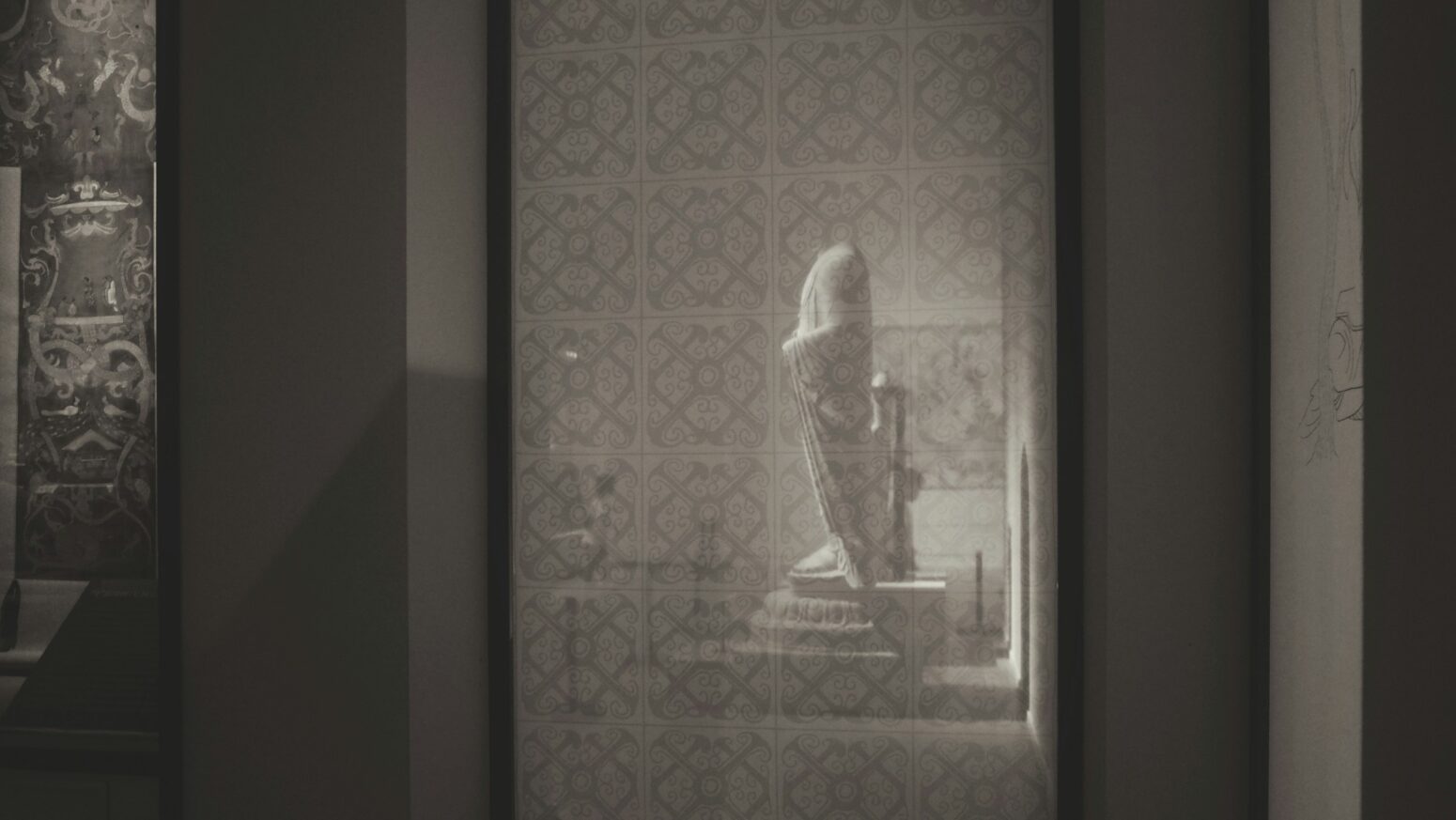 A headless statue either seen in reflection or through a glass panel.