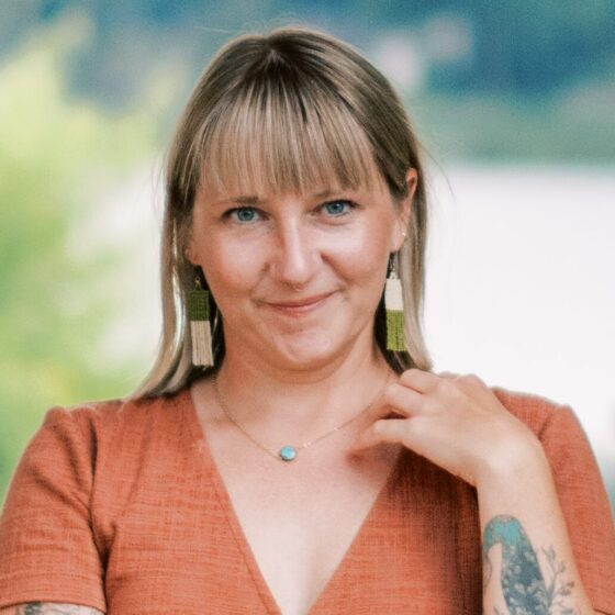 Headshot of Whitney Waters. She is wearing an orange top and green and white tassel earrings.