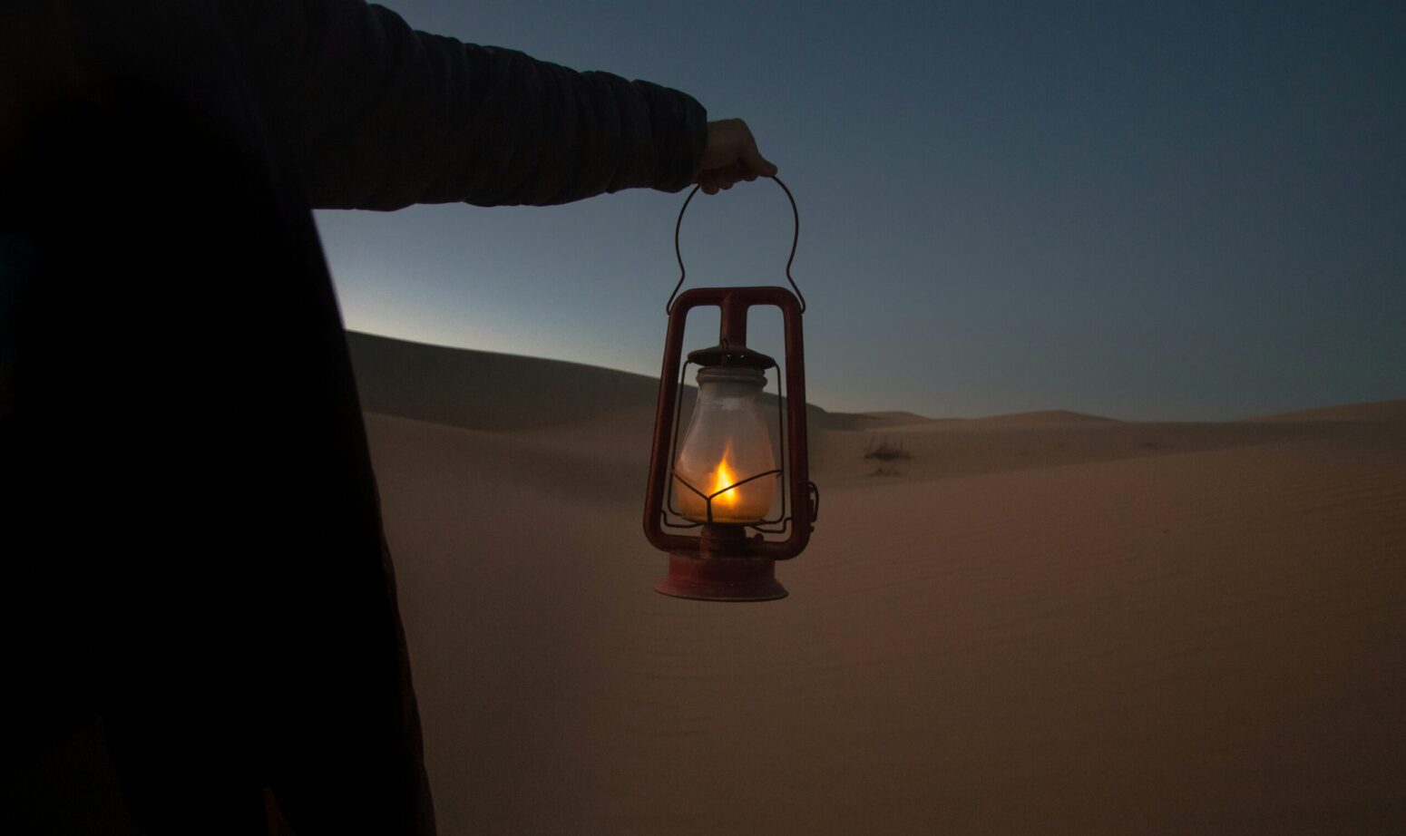 A woman walking on sand dunes while carrying a burning lantern.