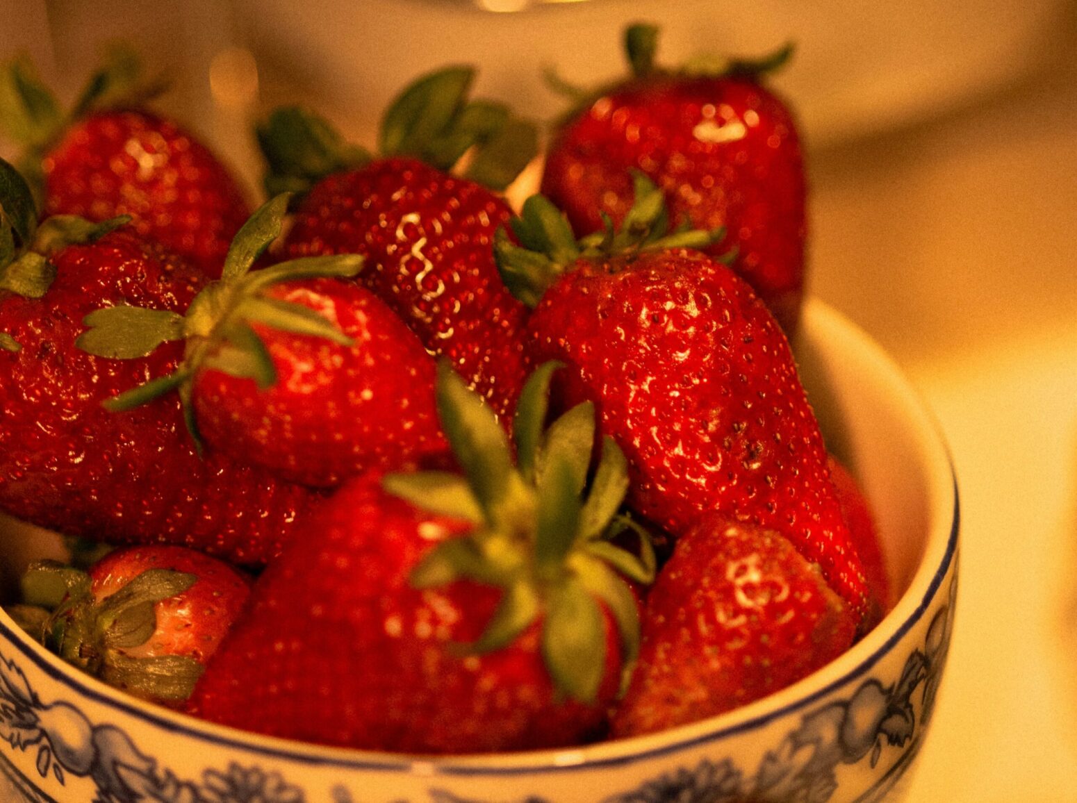 A bowl of strawberries sitting on the counter under yellow lighting