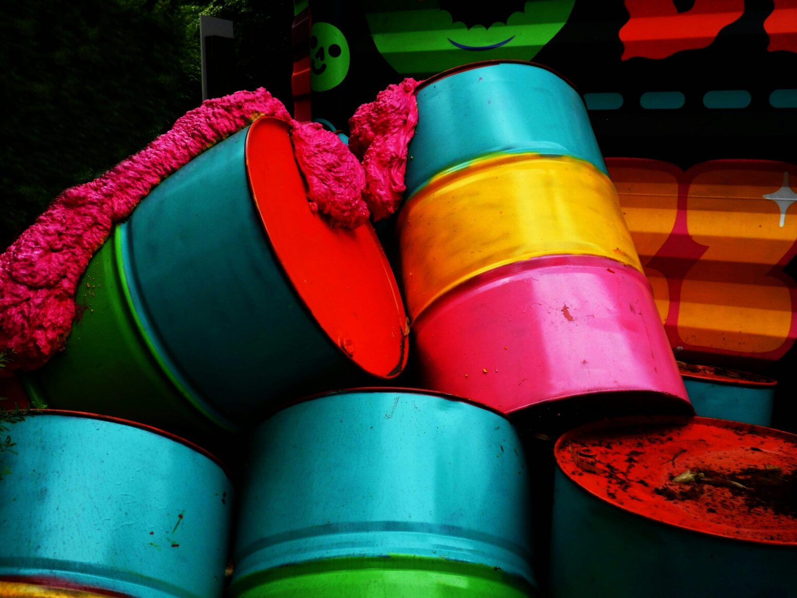 Stacks of brightly-colored, metal barrels, oozing some sort of pink substance.