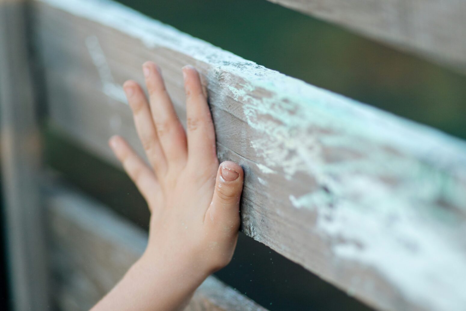 A white child pressing their hand up to an old, wooden fence.
