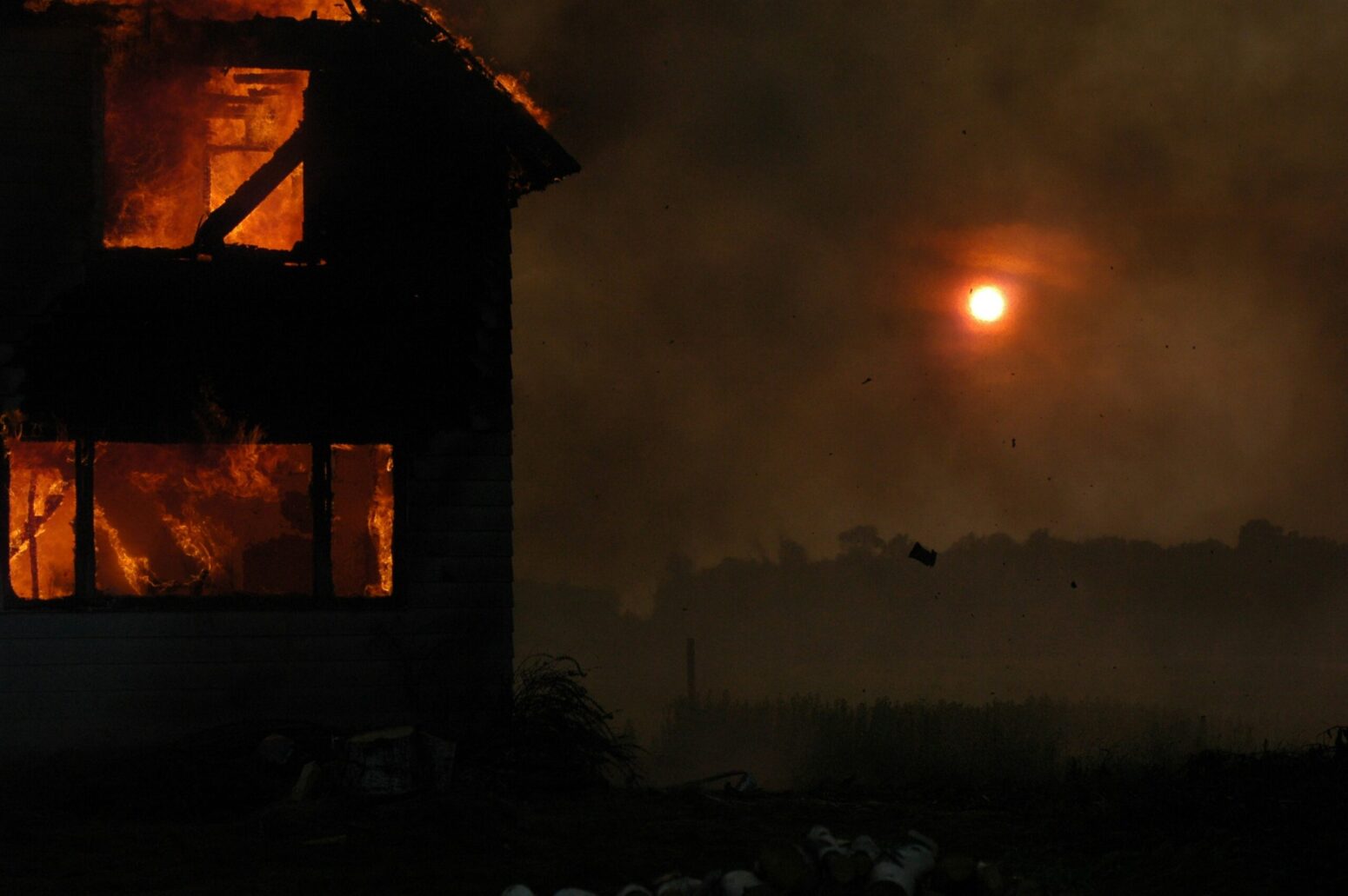 A wooden house on fire during the night. The color of the orange color of the flames matches the moon.