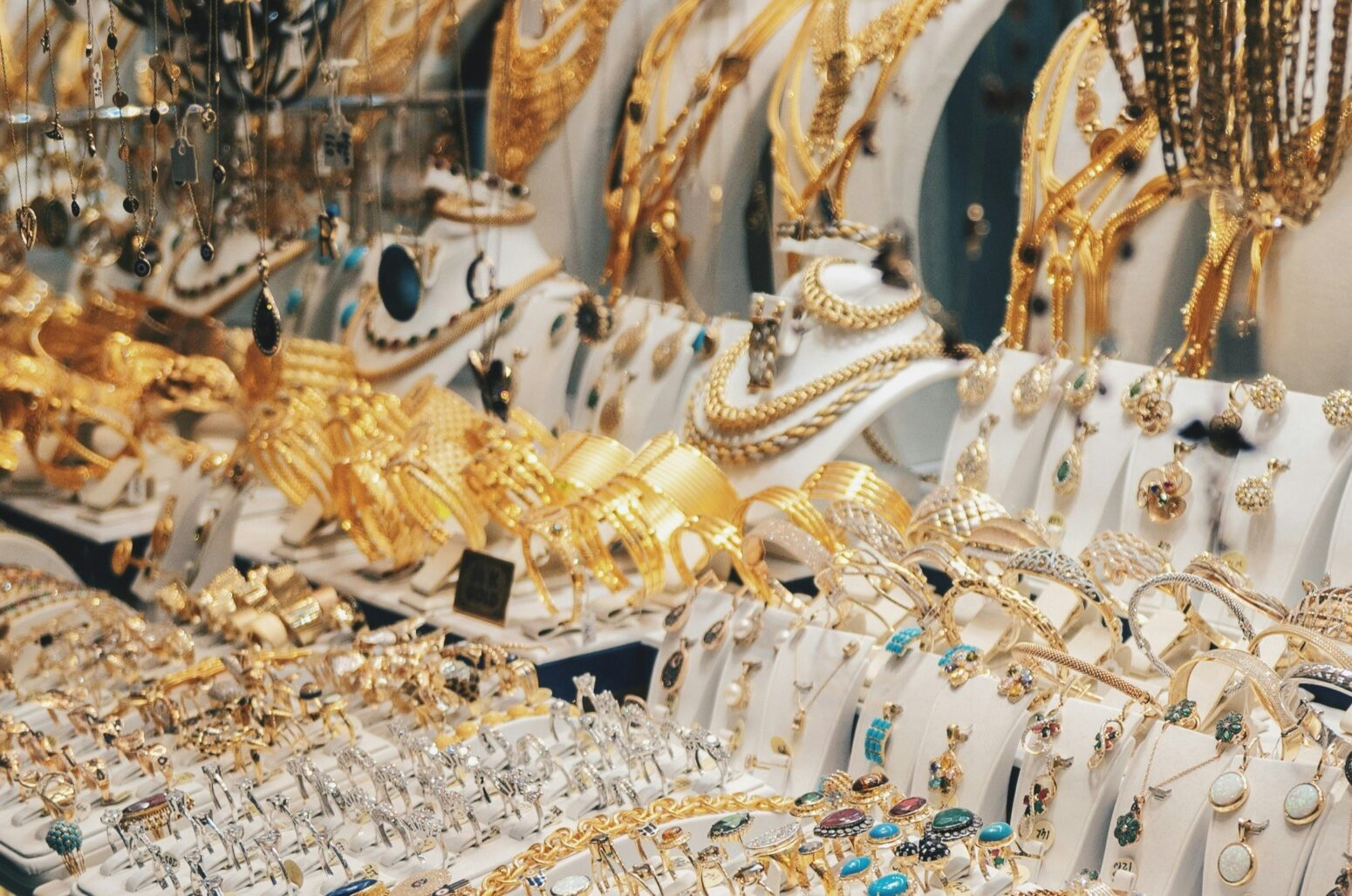 A very busy display of golden jewelry. There are bracelets, rings, and necklaces hanging and sitting on white, felt displays.