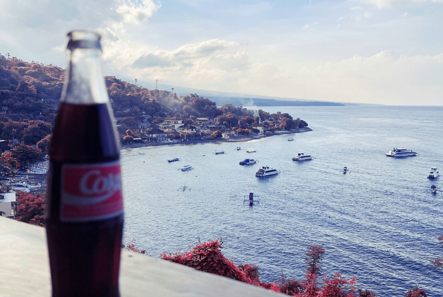 A view of a harbor with various ships in it. A glass bottle of Coca-Cola sits on the ledge to the left.