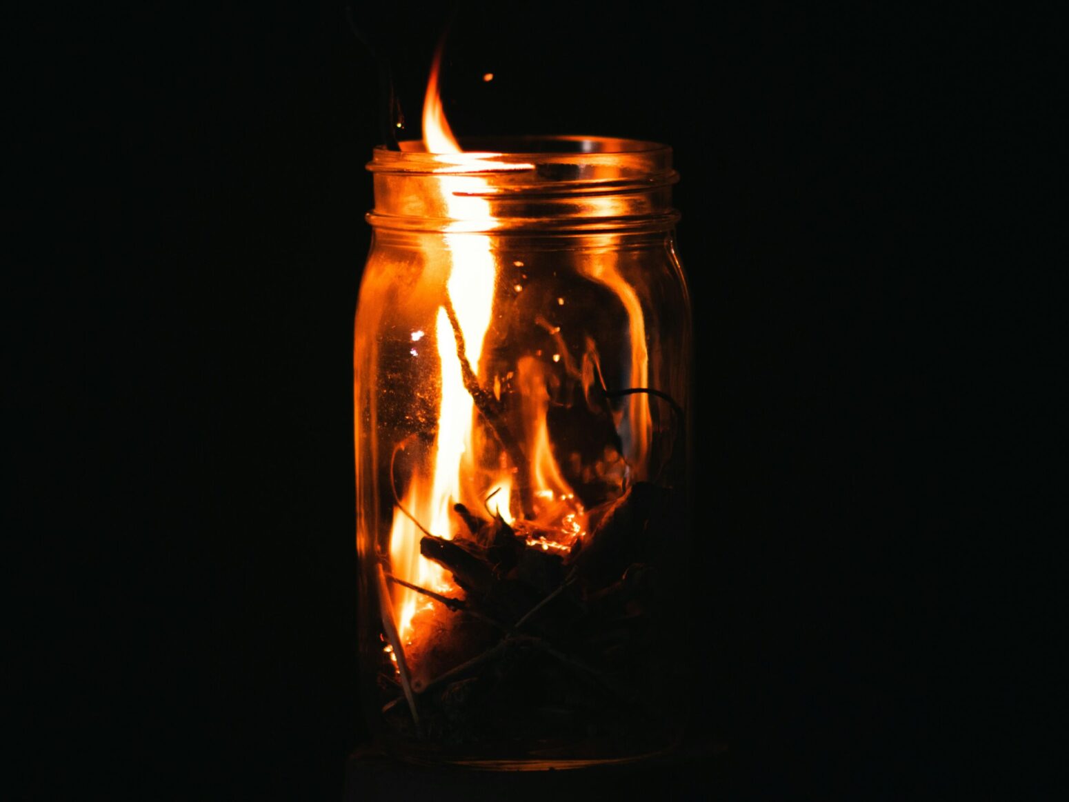 A burning pile of leaves in a glass jar on a black background.