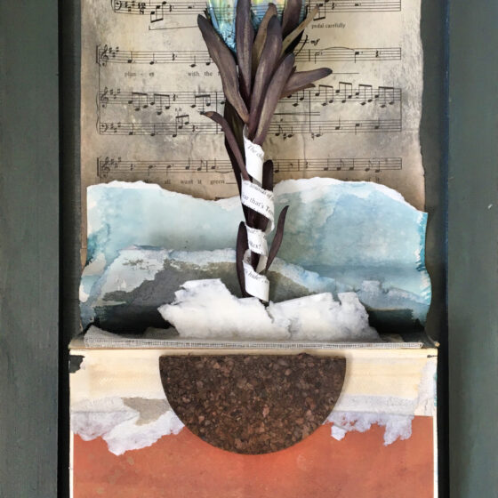 A gray, wooden frame surrounds this piece. At the top is a piece of sheet music titled "7. We're Sharing this Planet." In front of the sheet music, is a colorful flower that has the music imprinted on its petals. The stem of the flower is made out of dried plants, and a piece of paper with words around it wraps around it. The flower looks like it grows out of a blue, white, and gray-colored ground. Underneath the ground are a few thin, wooden panels, and then a red background. The roots of the flower are brown and black, and in a half-circle shape.
