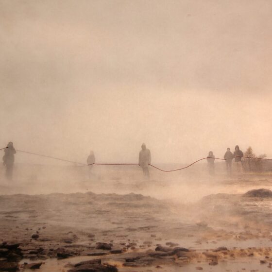 Sepia image of figures in a misty, rocky landscape. Sewn onto the image itself in red thread, a rope that each figure appears to be holding.