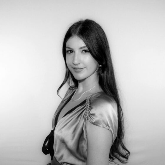 Black and white side profile photo of a woman. Her long hair is parted down the middle, and she is smiling softly.