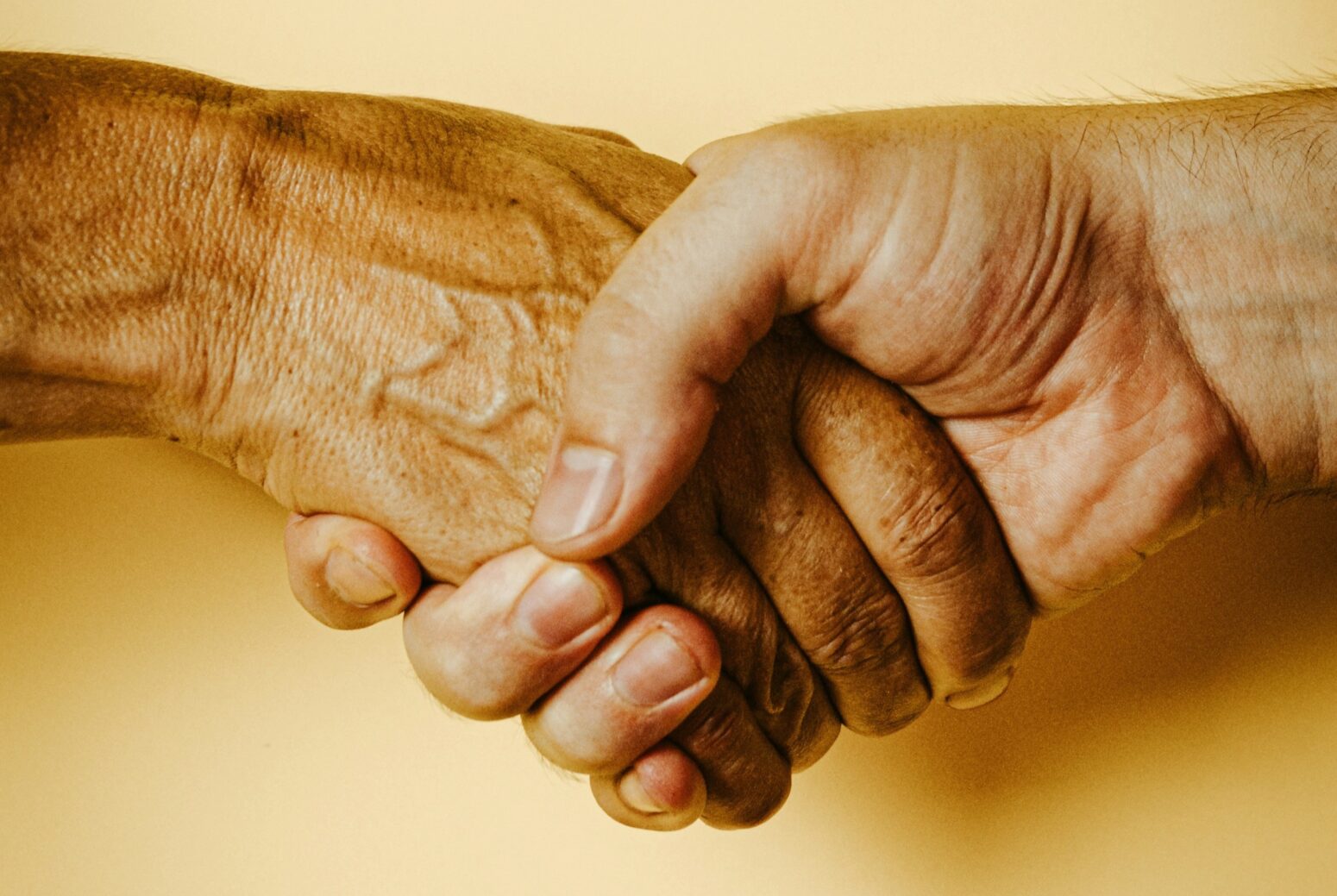 A close-up of two people grasping hands against a yellow background.